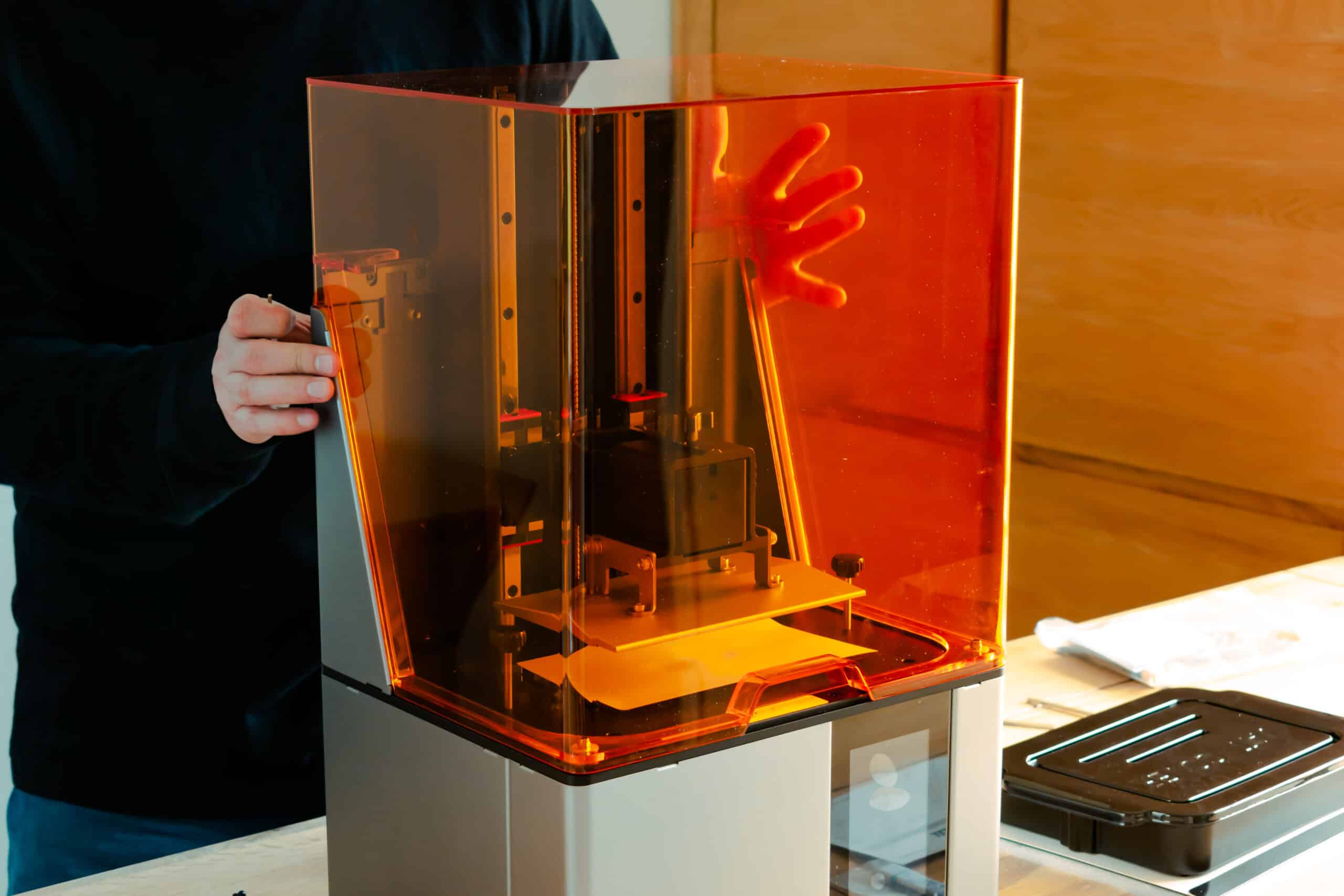 Person setting up a resin 3D printer before first use, hands near the machine and open vat