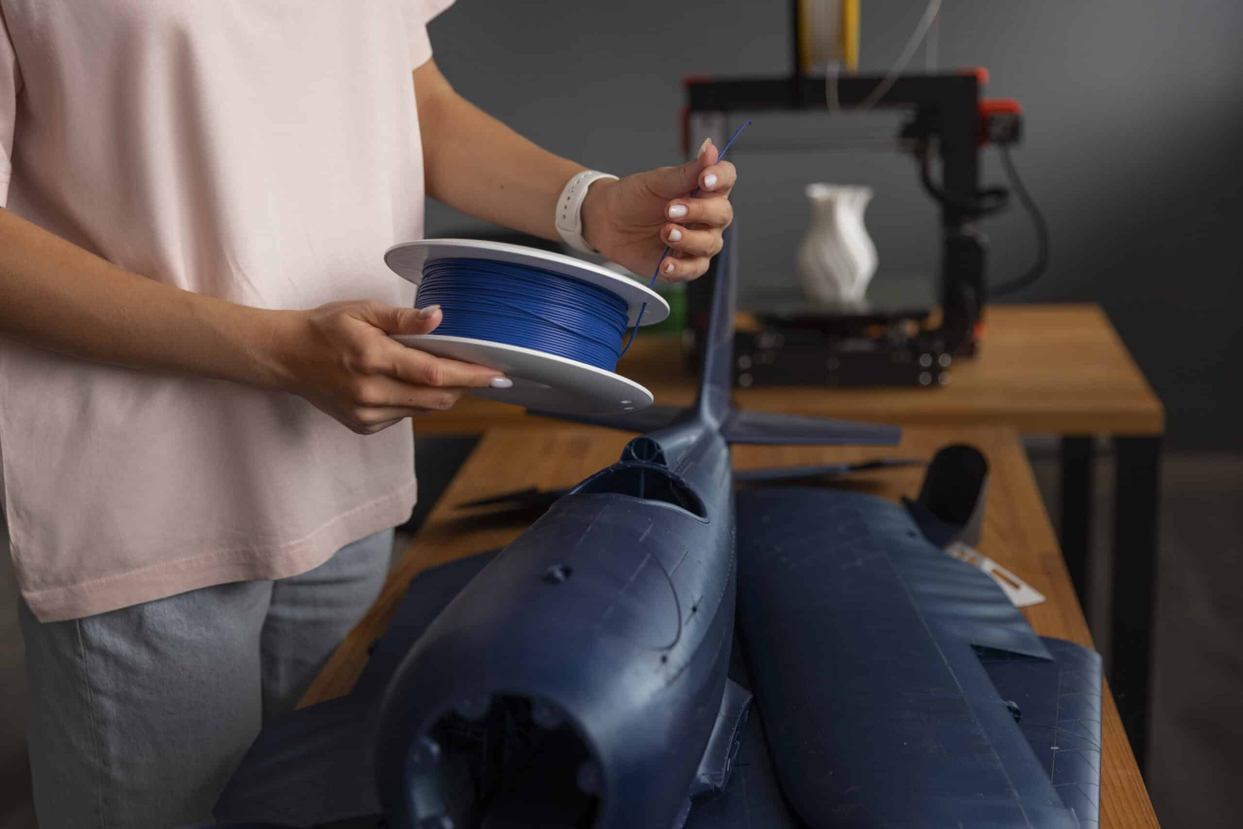 Person checking a 3D printer mid-print for curling on thin, flat features