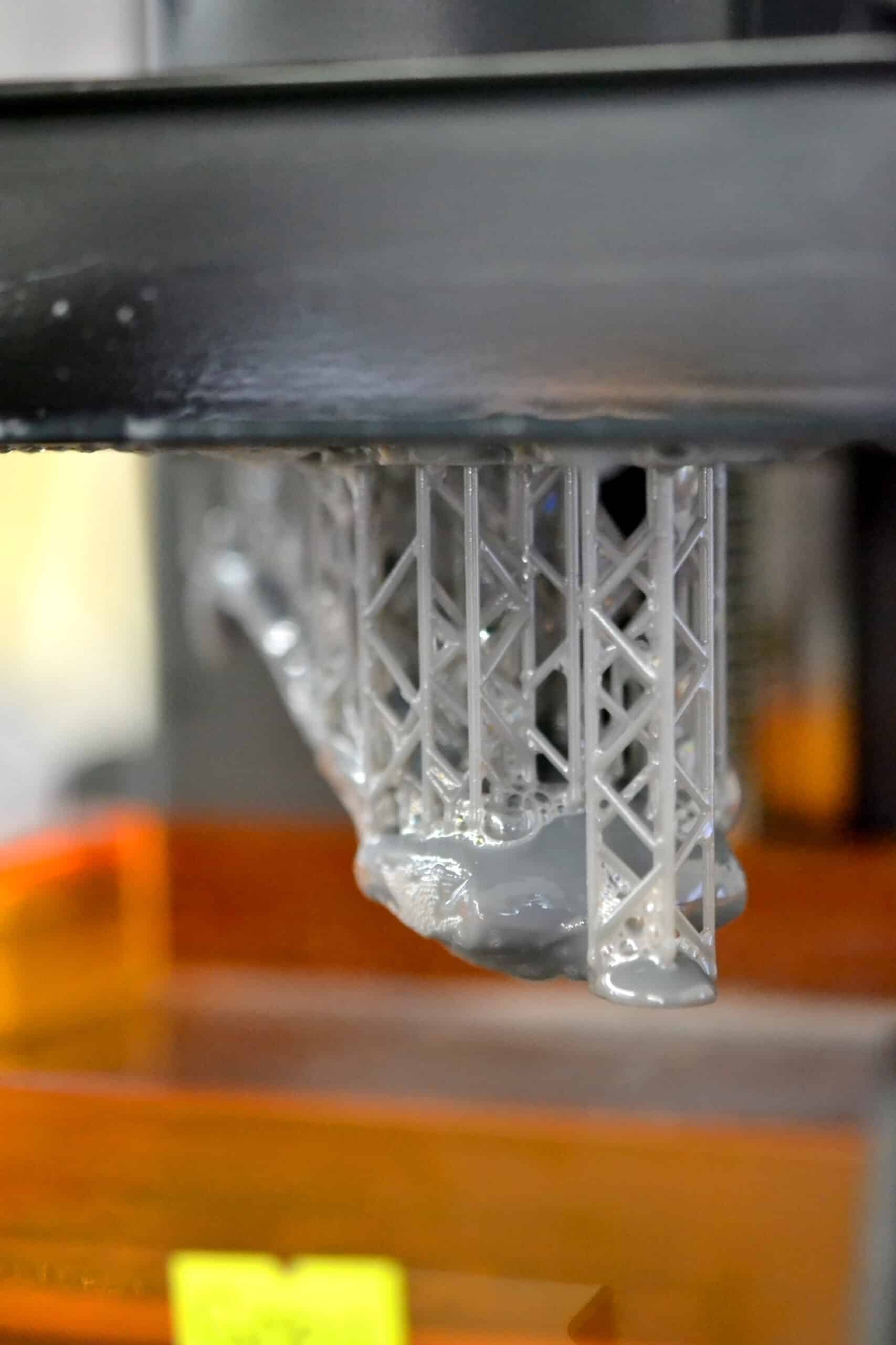 Close-up of a resin SLA 3D printer's build platform moving through liquid resin during a print, with resin drips visible