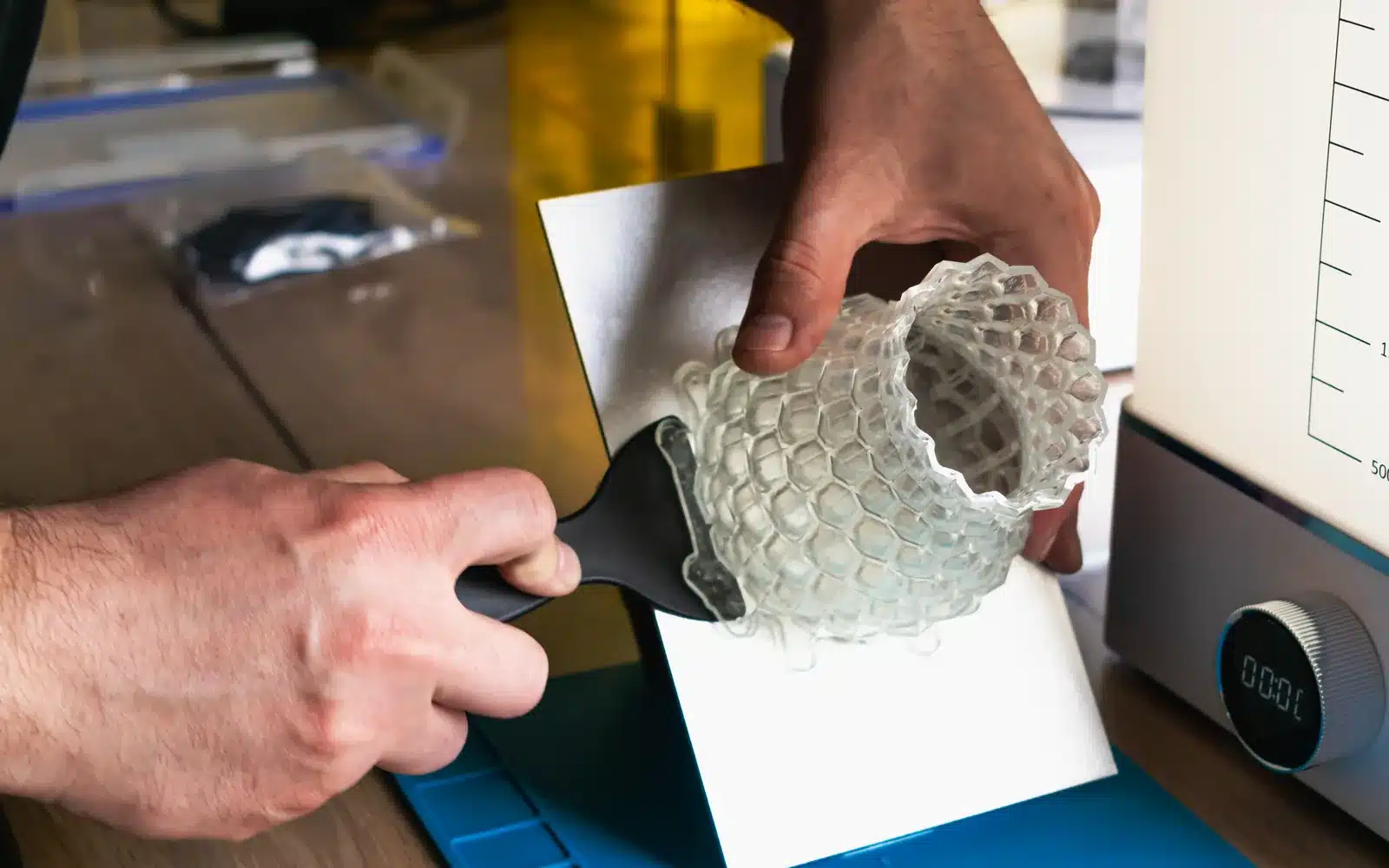 Maker handling a printed object beside enclosed resin equipment