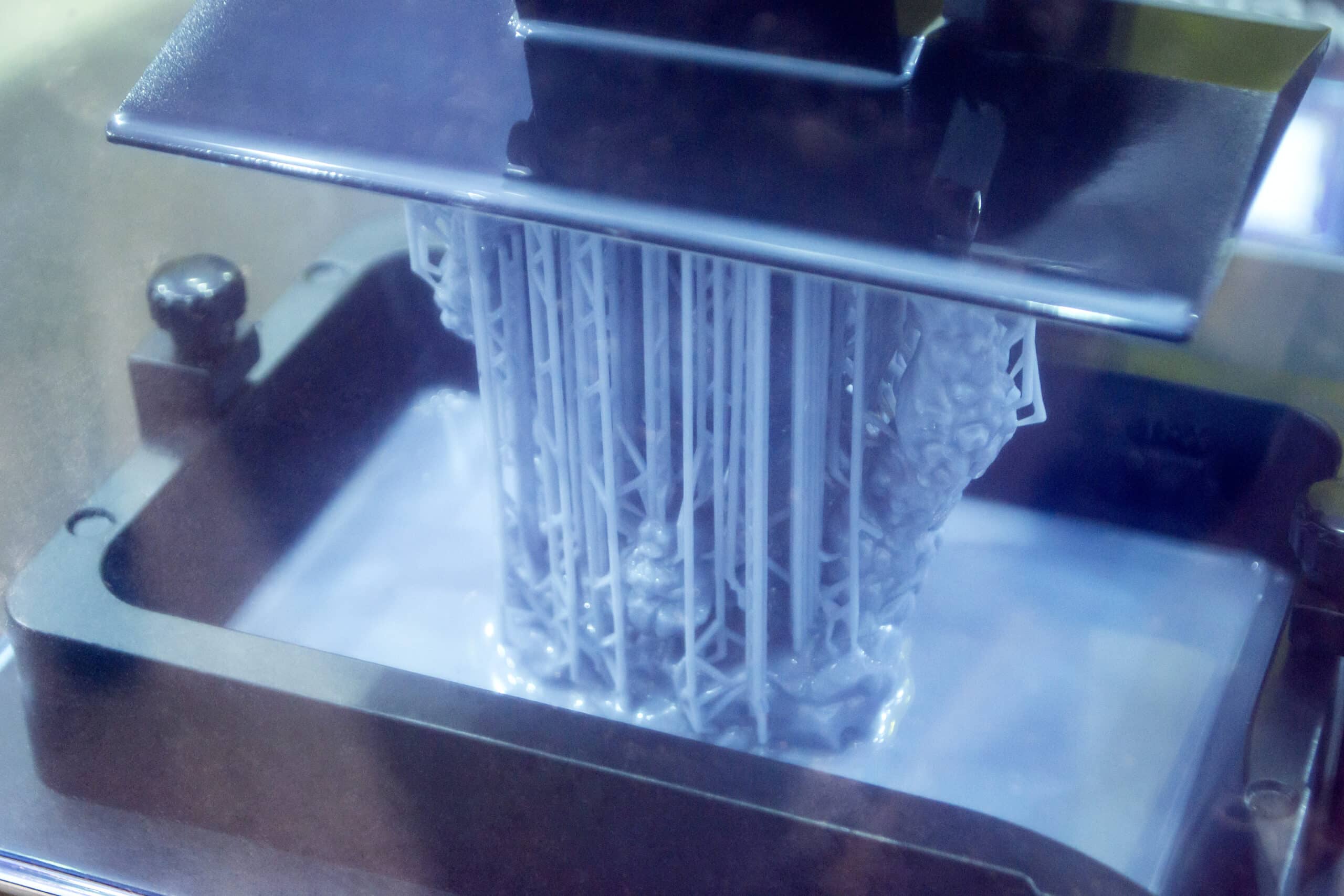 Close-up of a resin 3D printer's build platform lowering into the liquid photopolymer vat