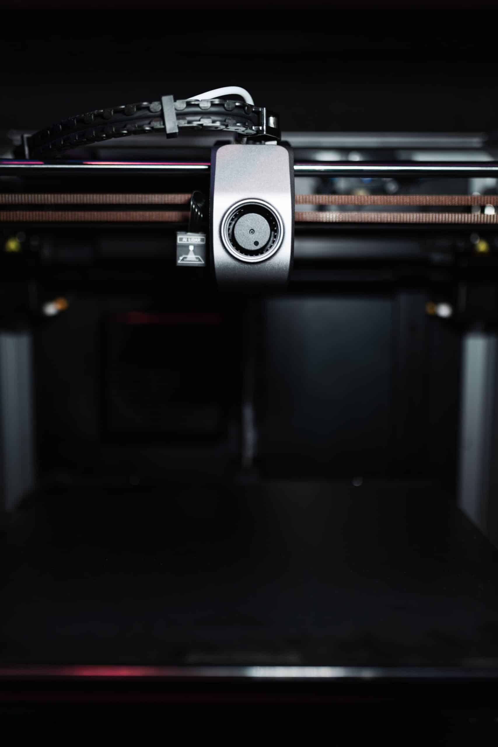 Close-up of a high-precision industrial 3D printer nozzle in a dark setting, showcasing advanced technology