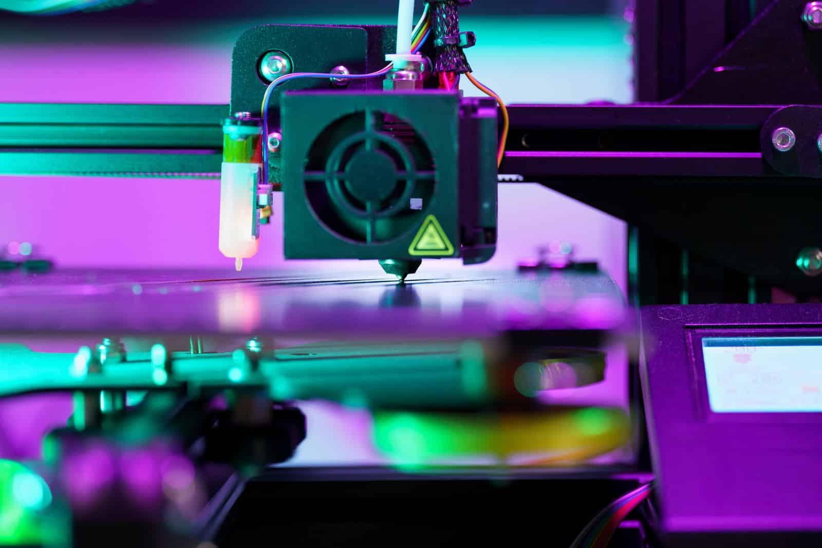 Neon-lit 3D printer nozzle in action, close-up