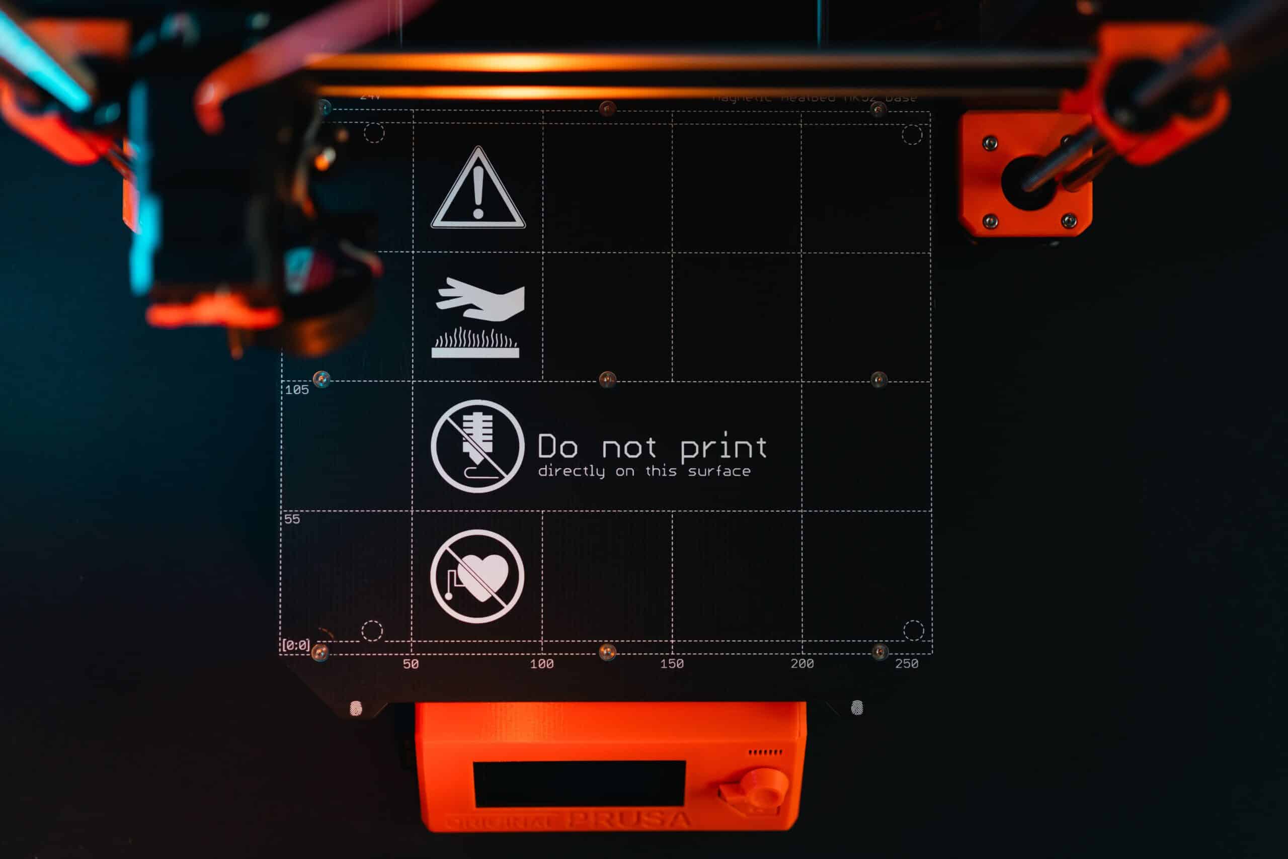 3D printer build plate with warning symbols, showcasing high-tech equipment in a workspace