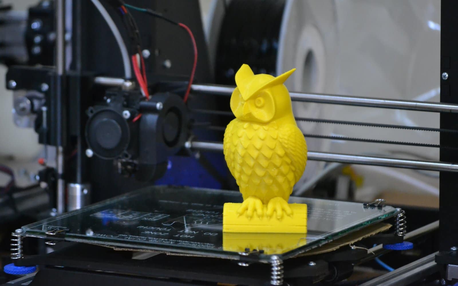 Close-up of a 3D printer nozzle depositing yellow plastic filament during a print.
