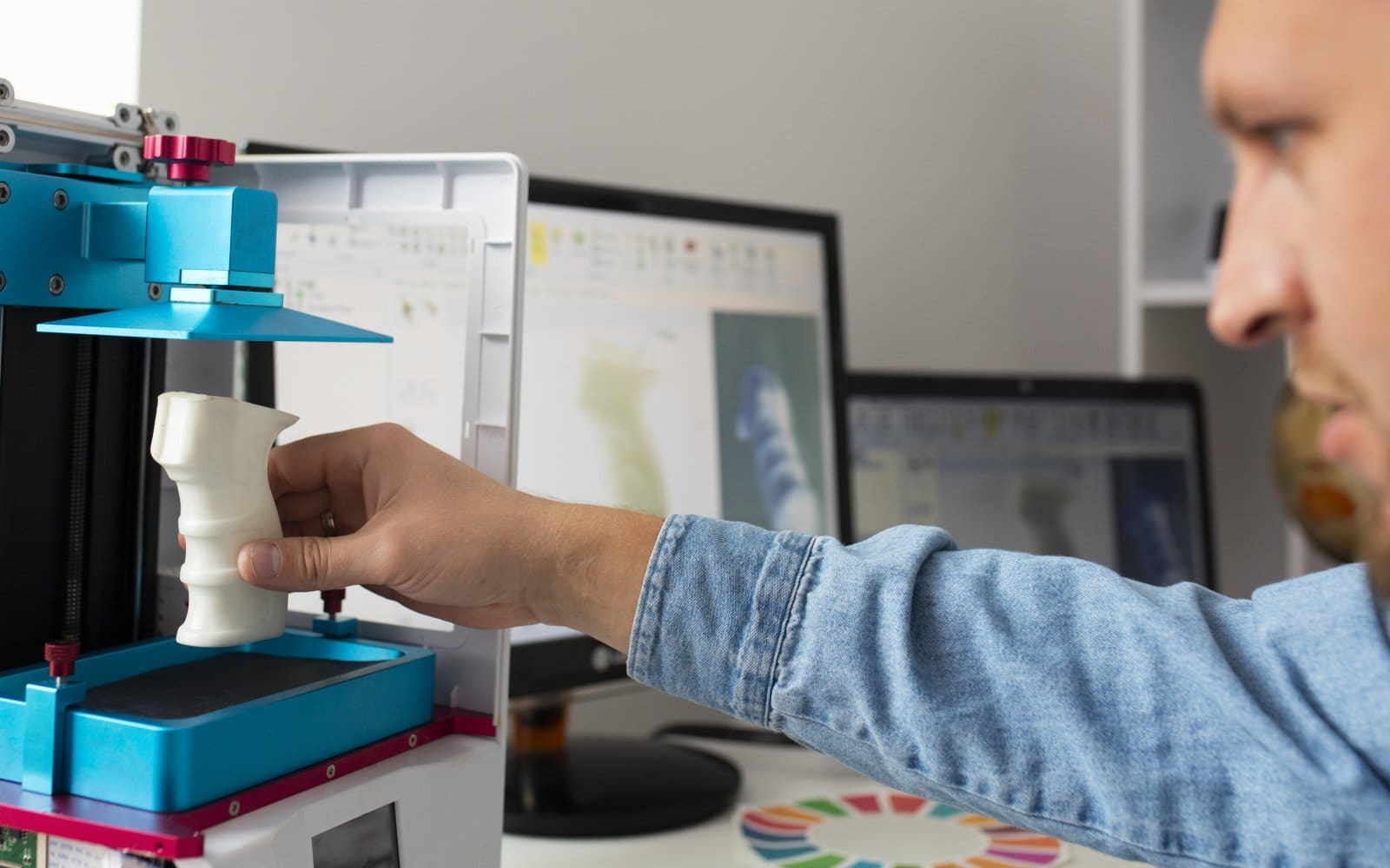 A person adjusting a desktop 3D printer near its build plate during calibration.