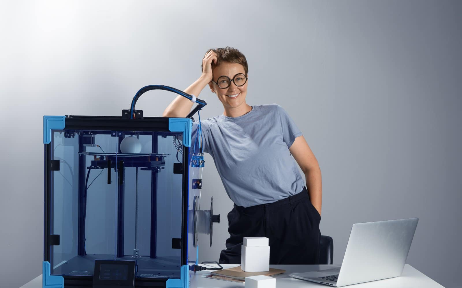 A person setting up a 3D printer on a desk in an office workspace.