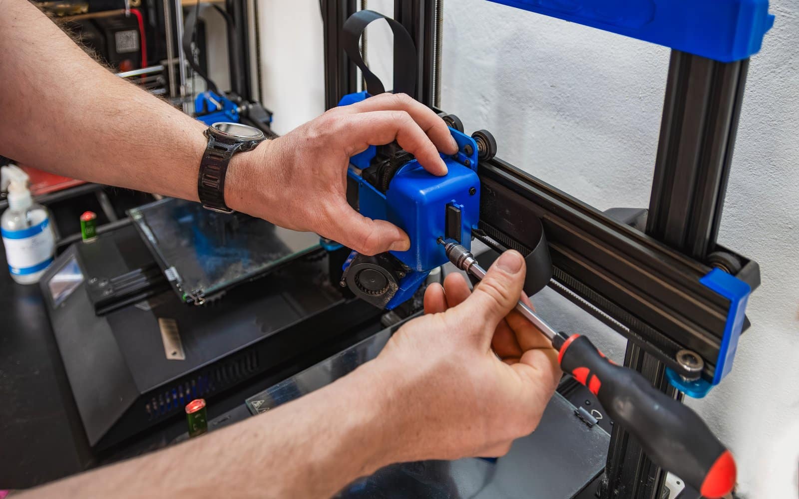 A technician's hands performing maintenance on a 3D printer.